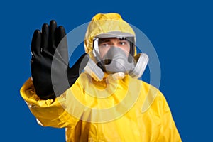 Man in chemical protective suit making stop gesture against background, focus on hand. Virus research