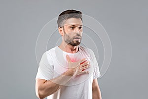 Man with chest pain touching inflammated zone, grey background