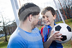 Man with child playing football on pitch