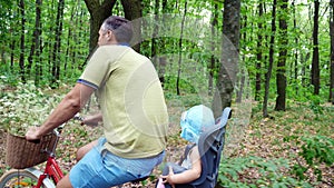 A man with a child riding a bicycle in the forest, in the summer, the child is sitting in a special chair