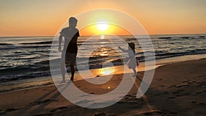 Man and child run along the beach at sunrise.