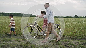 A man with children rides a retro bike. A family with a bicycle is resting on a flower field. Retro style. A fashionable bicycle