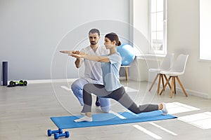 Man chiropractor fixing woman patients movements during exercising on fitness mat