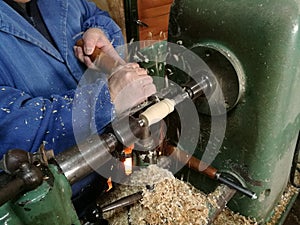 Man chiseling a wooden cylindrical block pinned in between of the shaft of a rotary machine