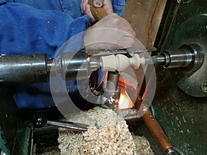 Man chiseling a wooden cylindrical block pinned in between of the shaft of a rotary machine