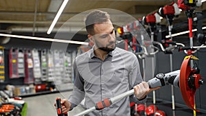 A man chooses an electric trimmer for mowing lawn grass in a gardening equipment store