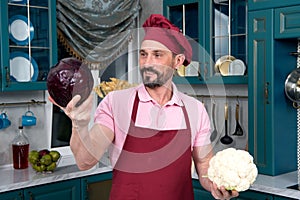 Man chooses vegetables for cooking. Happy chef make chose between fresh red cabbage and cauliflower for salad. Cabbage and caulifl