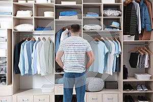 Man choosing outfit from large wardrobe closet with clothes, shoes and home stuff photo