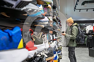 Man choosing variety of sneakers in store, examining pair in hands. Shopping culture, choice, and fashion trends photo