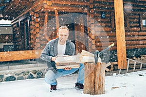 Man chopping wood on snowy yard for a house fireplace with heavy snowflakes background . Winter countryside holidays concept image