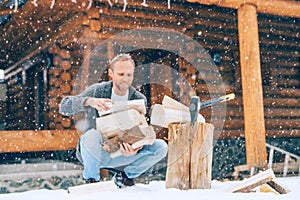 Man chopping wood on snowy yard for a house fireplace with heavy snowflakes background . Winter countryside holidays concept image