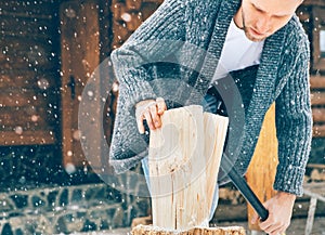 Man chopping wood on snowy yard for a house fireplace with heavy snowflakes background . Winter countryside holidays concept image