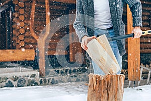 Man chopping wood on snowy yard for a house fireplace with heavy snowflakes background . Winter countryside holidays concept image