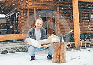 Man chopping wood on snowy yard for a house fireplace with heavy snowflakes background . Winter countryside holidays concept image