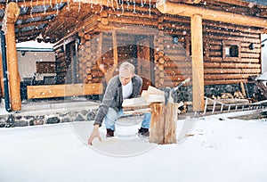 Man chopping wood on snowy yard for a house fireplace with heavy snowflakes background . Winter countryside holidays concept image