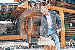 Man chopping wood on snowy yard for a house fireplace with heavy snowflakes background . Winter countryside holidays concept image