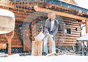 Man chopping wood on snowy yard for a house fireplace with heavy snowflakes background . Winter countryside holidays concept image