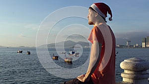 Man in the Christmas cap sits on the railing and looking at fishing boas in sea and raising sun