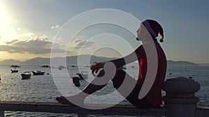 Man in the Christmas cap sits on the railing and looking at fishing boas in sea and raising sun