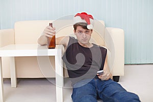 Man in christmas hat sits on a floor with beer