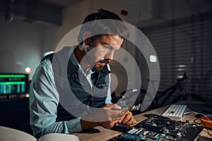 Man, circuit and it repair workshop in night for maintenance, computer tech or industry with focus. Technician