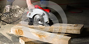 Man with circular saw for cutting boards. Construction and home renovation in the workshop. Worker saws a wooden plank