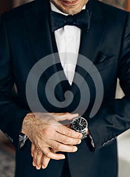 A man in a classic suit and bow tie is wearing a wrist watch