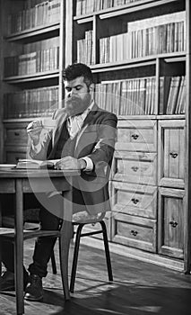 Man in classic suit sits in vintage interior, library, book shelves on background. Aristocratic lifestyle concept