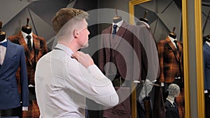 A man in a classic white shirt puts on a tie. Businessman looks in the mirror in a men`s clothing store against the backdrop of su
