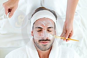 Man with clay facial mask in beauty spa.