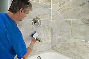 Man cleaning bathtub tiles and fixtures with scrub brush photo