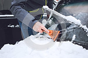 Man cleaning car from snow and ice with brush and scraper tool during snowfall. Winter emergency. Weather-related vehicle