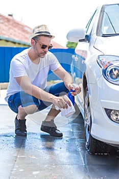 Man cleaning car wheel with cloth and spray bottle