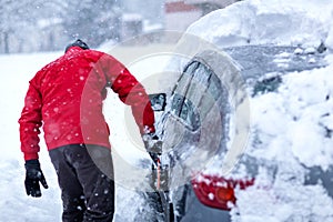 Man cleaning car windows from snow in winter season