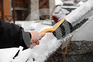 Man cleaning car windshield from snow with brush outdoors