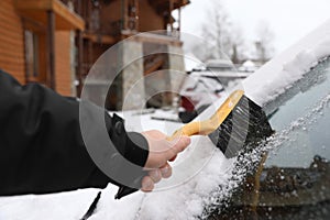 Man cleaning car windshield from snow with brush outdoors