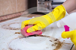 Man cleaning ceramic modern stove or hob with detergent agent. Hand in yellow gloves clean stove from burnt and grease dirt.