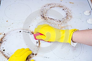 Man cleaning ceramic modern stove or hob with detergent agent. Hand in yellow gloves clean stove from burnt and grease dirt.