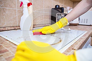 Man cleaning ceramic modern stove or hob with detergent agent. Hand in yellow gloves clean stove from burnt and grease dirt.