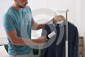 Man cleaning clothes with lint roller indoors, closeup