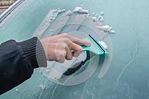 Man is cleaning frozen car window with ice scraper.