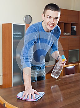 Man cleaning furniture with cleanser and rag at living room