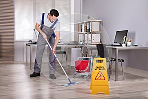 Man Cleaning Hardwood Floor In Office