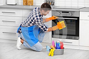 Man cleaning kitchen oven with rag