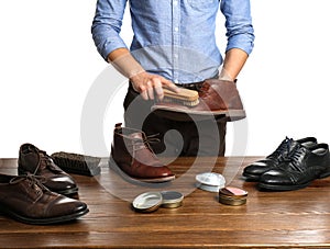 Man cleaning leather shoe at wooden table against white background,