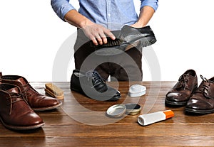 Man cleaning leather shoe at wooden table against white background