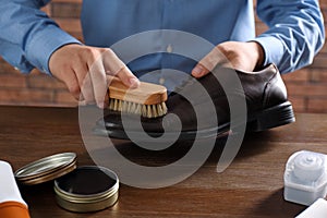 Man cleaning leather shoe at wooden table, closeup