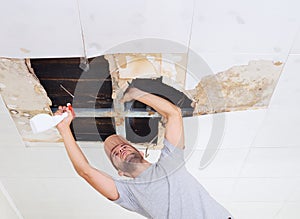 Man cleaning mold on ceiling.Ceiling panels damaged huge hole in