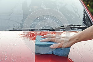 Man cleaning red automobile with blue sponge at car wash wite copy space for text