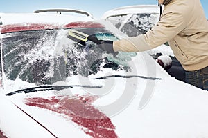 Man cleaning snow from car windshield with brush